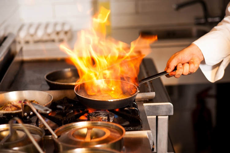 повар держит сковороду с горящим огнём